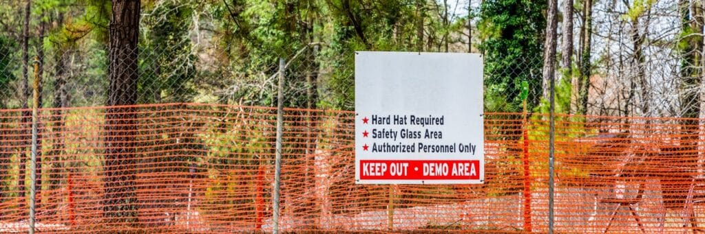 Orange construction safety fencing and warning sign protecting trees near a wooded construction site.