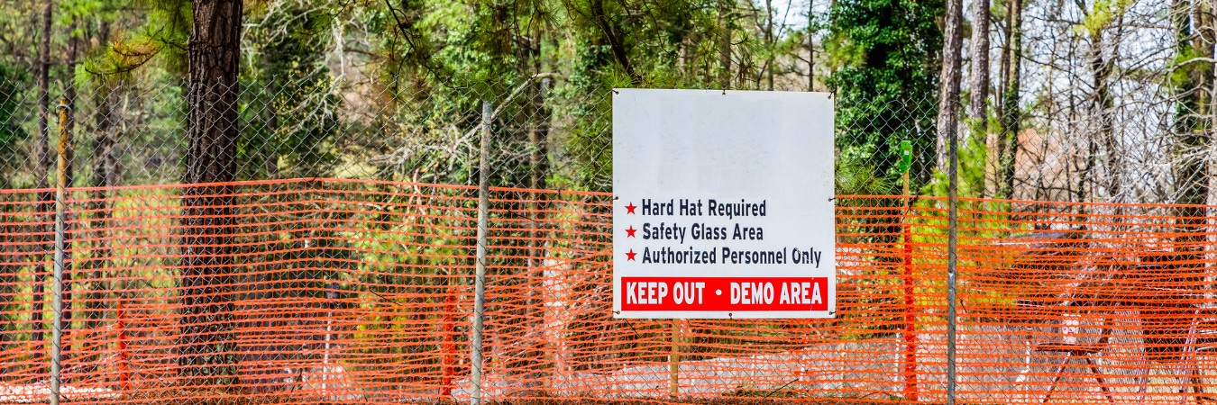 Orange construction safety fencing and warning sign protecting trees near a wooded construction site.