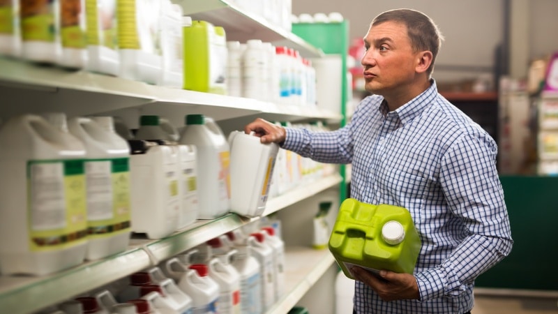 A plant health care technician selecting specialized treatment products from organized shelves in a storage facility.